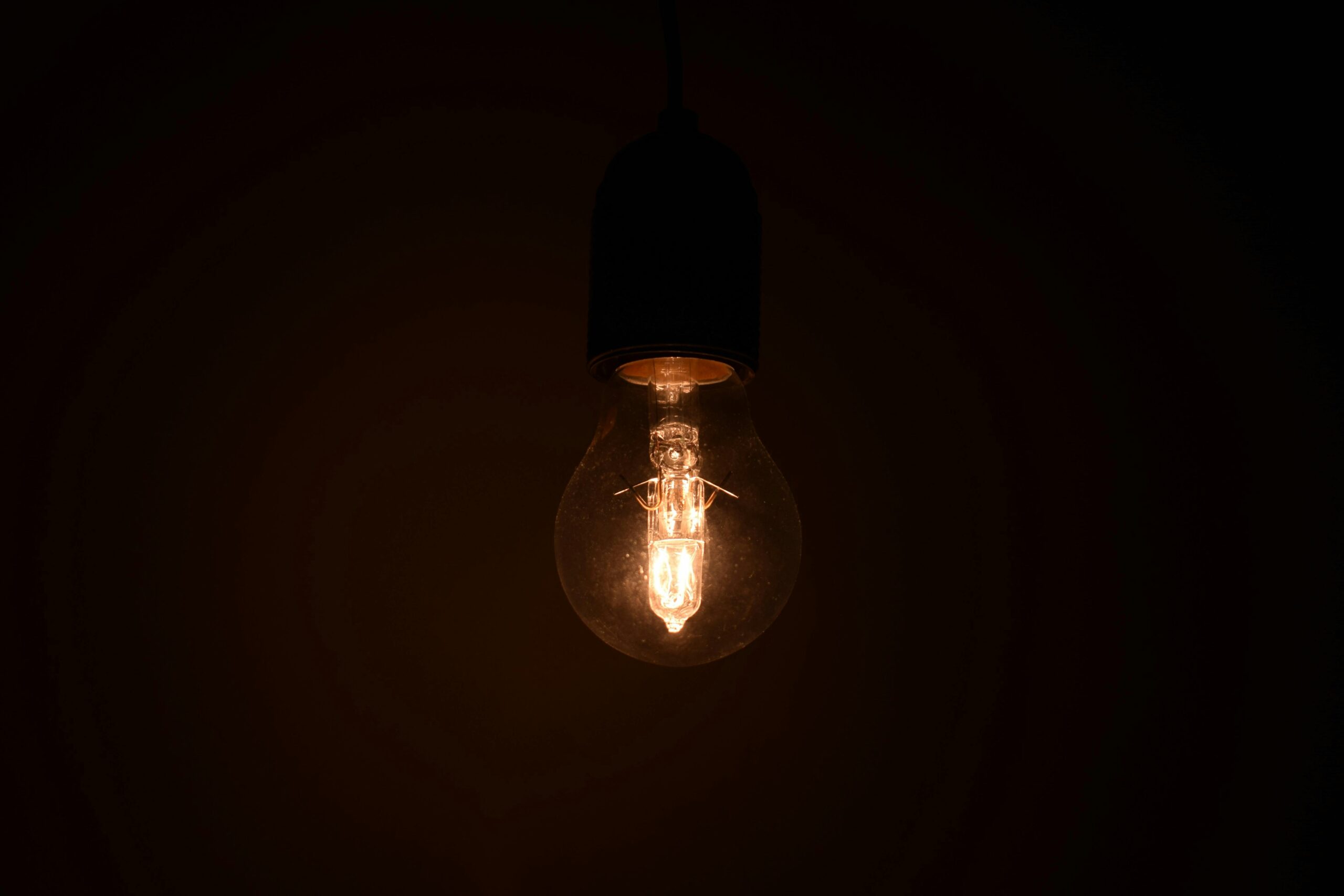 Close-up view of an illuminated light bulb glowing in a dark environment, emitting warm light.